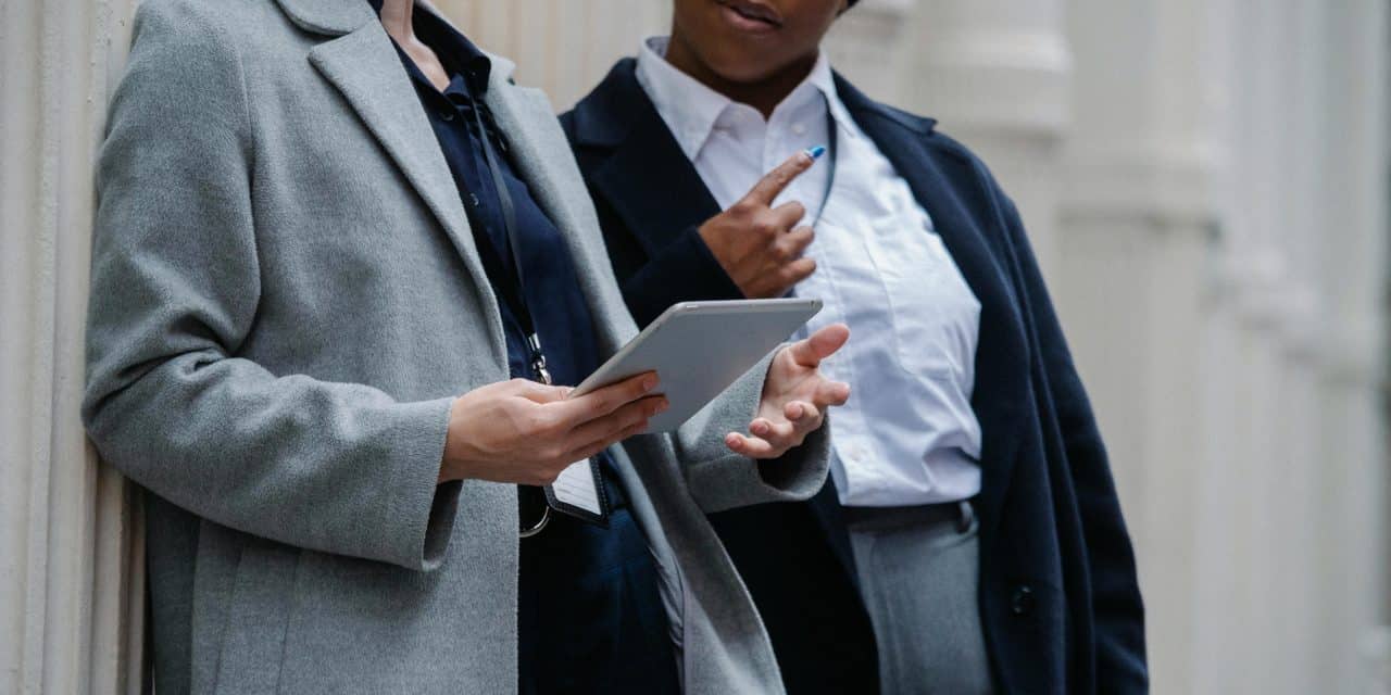 Two women wearing ID badges discussing information on a tablet
