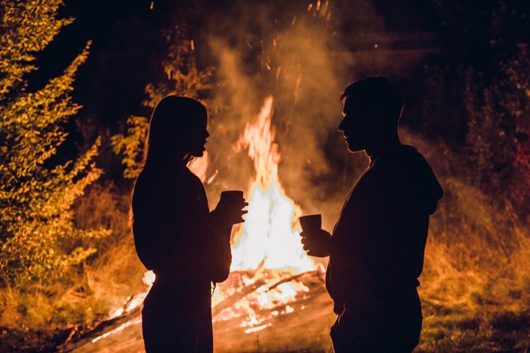 two people standing near a bonfire at night.