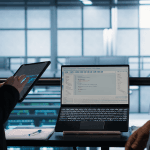 two professionals collaborating with laptop and tablet displaying code and technical data