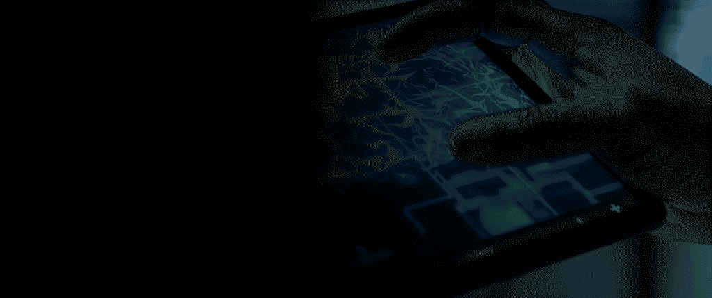 close-up of hands interacting with a digital tablet touchscreen displaying a grid interface in dramatic blue-tinted low lighting against a dark background