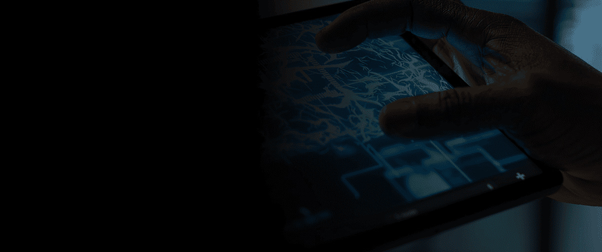 close-up of hands interacting with a digital tablet touchscreen displaying a grid interface in dramatic blue-tinted low lighting against a dark background