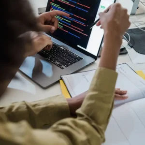 person typing code on a laptop in an office, colorful lines of code visible on the screen.