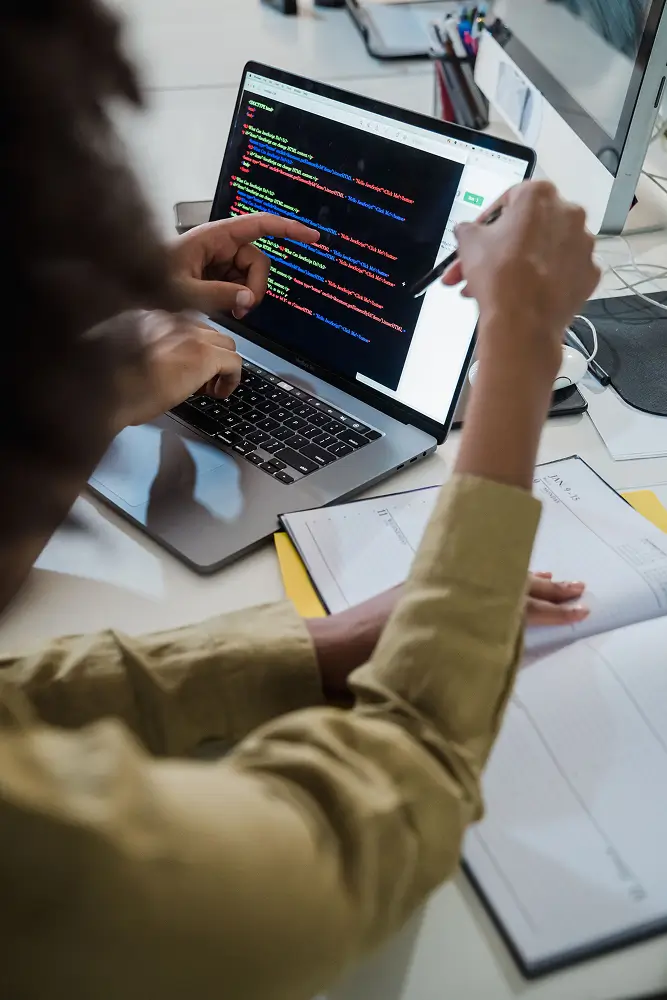 person typing code on a laptop in an office, colorful lines of code visible on the screen.